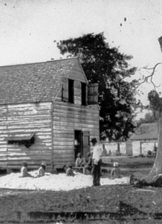 Photo of a United States Colored Troops soldier outside of a small wooden building.