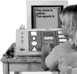 Photo: Girl using Intellikeys, a large keyboard with an overlay that has shapes, colors and some words on it. On her computer screen she has typed 'The circle is yellow. The square is' to describe some blocks to her left