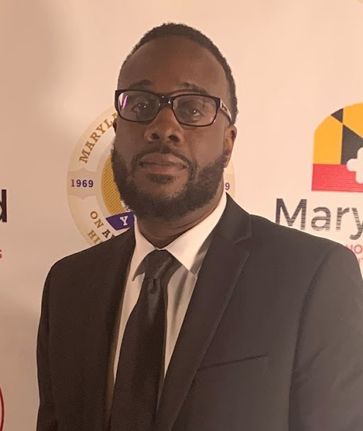 Photograph of Corey Lewis withe the Maryland state flag behind him.