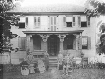 front of house with ornate ironwork and six people sitting outside